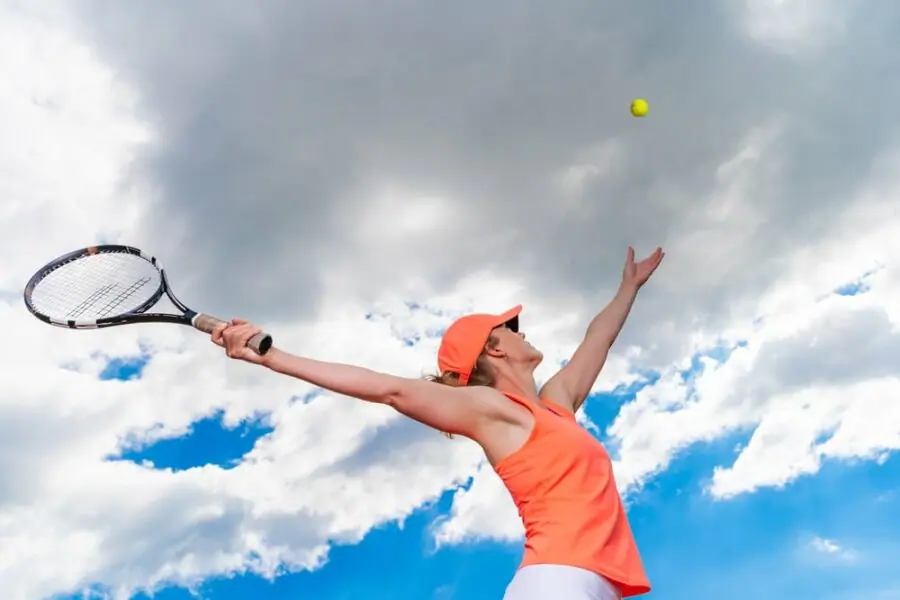 Woman tennis player reaches up to serve against a blue sky