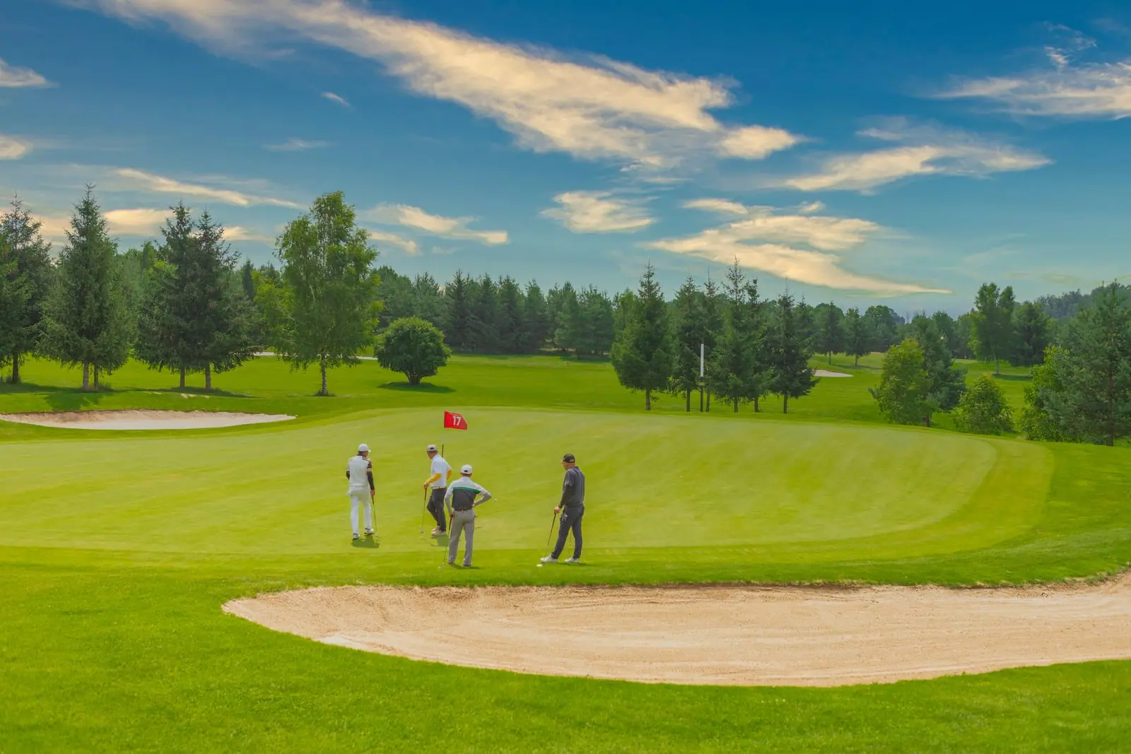 Golfers on a green beside a sand bunker