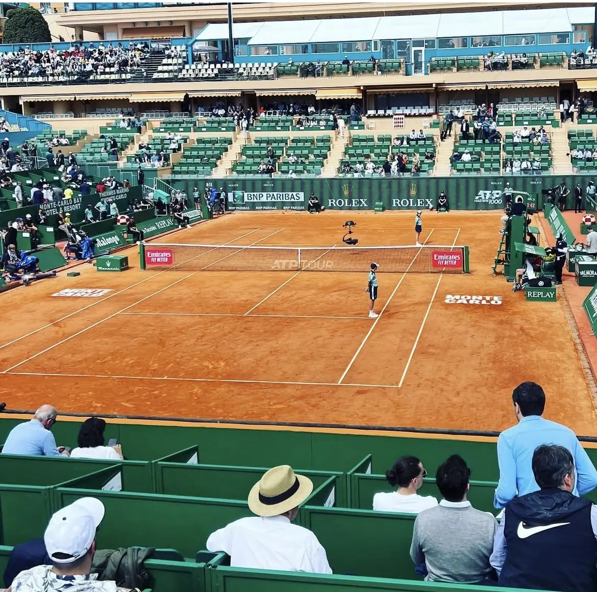 A tennis match in progress on a clay court with spectators