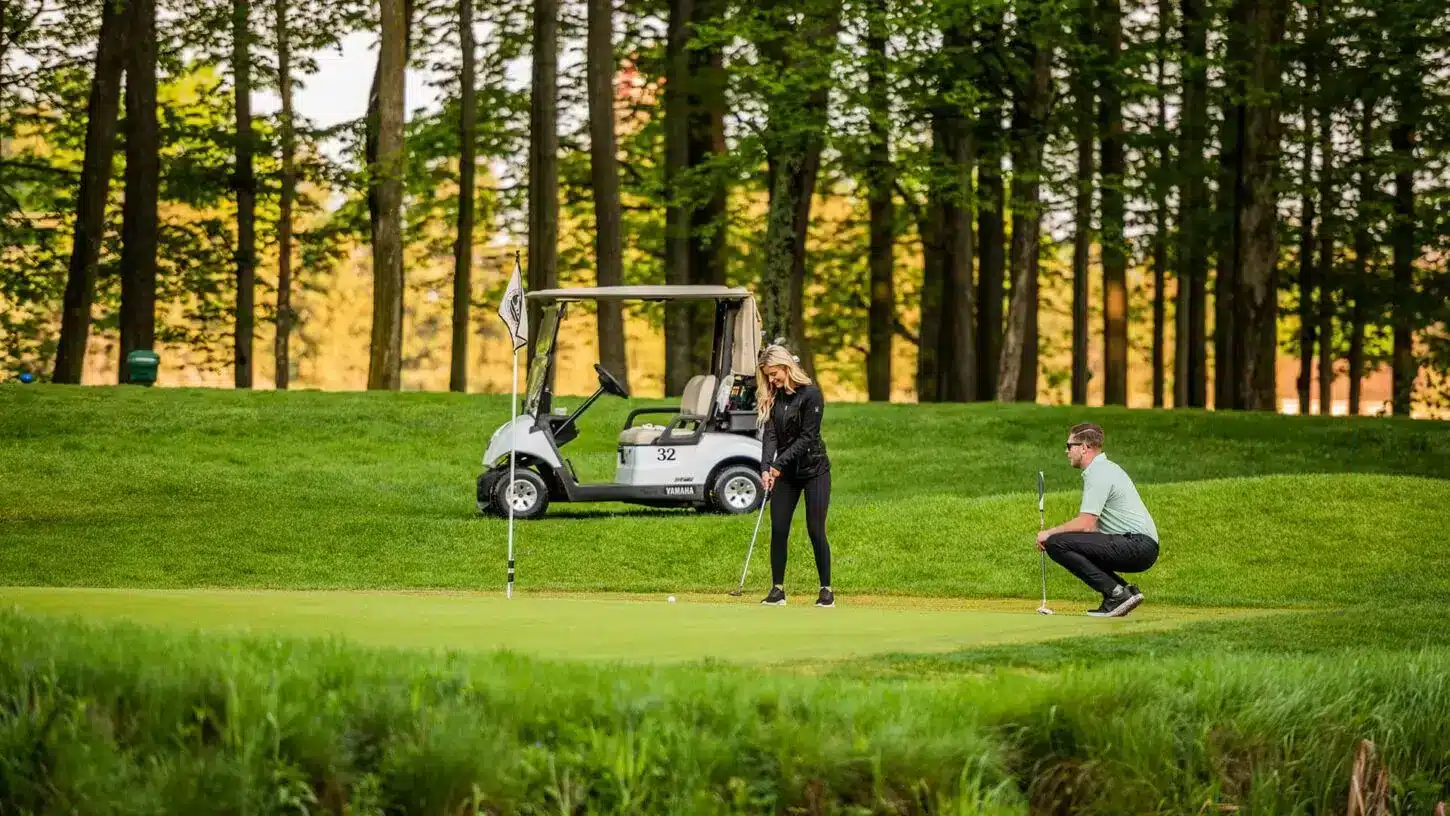 Golfers on a green with a golf cart beside the trees