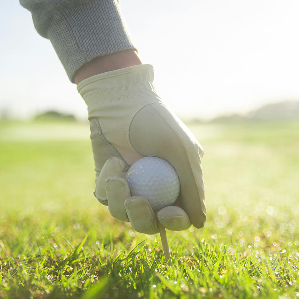 A golfer's hand setting up a golf ball on a tee in a grassy field