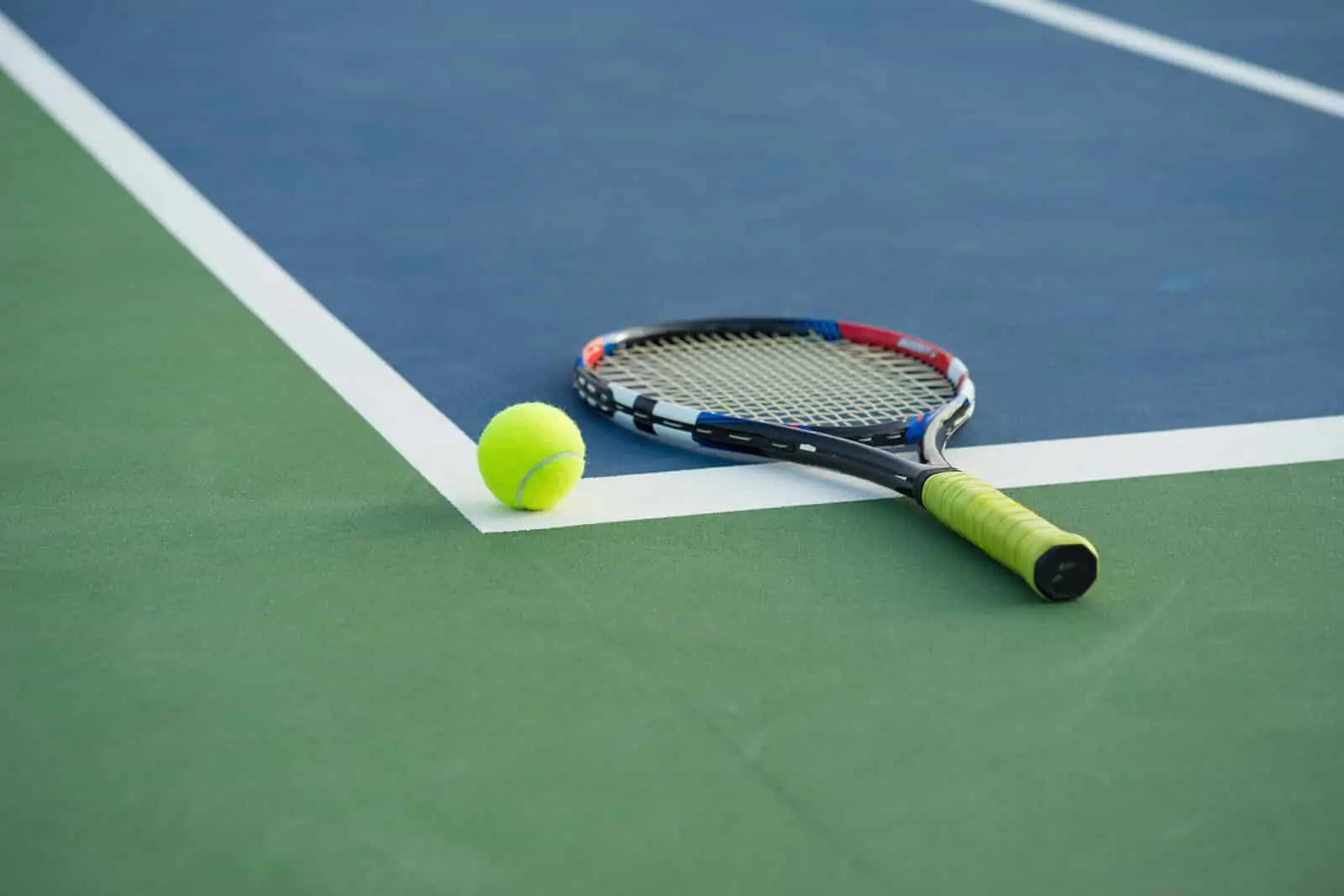 A tennis racket and ball on a blue hard court